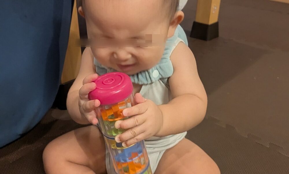 座っている赤ちゃんが両手でミニレインボーメーカーで遊んでいる